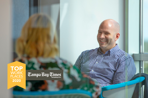 Man smiling while sitting across from a woman in conversation with Tampa Bay Times Top Workplaces 2020 logo overlayed