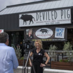 Woman in front of news camera with Deviled Pig storefront behind her