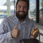 Male smiling for camera with food and giving the thumbs up