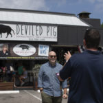 Man in front of news camera with Deviled Pig storefront behind her