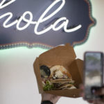 Person taking photo of their food in front of a sign that says "hola"