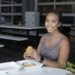 Woman sitting at restaurant table holding a sandwich and smiling for camera