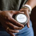 Woman holding a candle with lid that states "Blue Sage Candles"