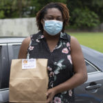 Woman holding brown paper food bag in front of car