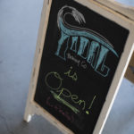 Sidewalk chalkboard that states "Tidal Brewing Co is open!"