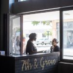 Wait staff talking at restaurant in front of mural that states "7th & Grove"