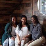 Group of three young woman sitting on bench smiling for camera