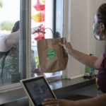 Woman handing a brown bag to a customer through a drive-thru window