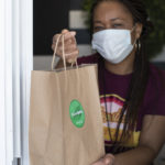 Woman in mask handing a brown bag through a drive-thru window