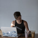 Young woman working at table with laptop and iced coffee