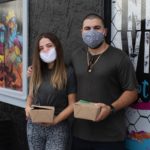 Young man and woman posing for camera with to-go box of food