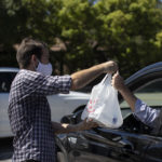 Man handing to-go food bag to driver in car