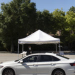 Parked white sedan vehicle in front of event tent