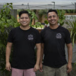 Two man smiling for camera in front of plants