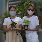 Two young woman holding plants and posing for camera