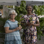 Two older woman holding plants and posing for camera