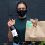 Woman in a green shirt posing for camera and holding bottle of wine