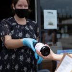 Cru Cellars store clerk handing a bottle of wine to customer