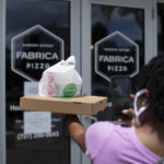 Woman holding a box of pizza walking into storefront