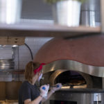 Woman placing pizza into brick oven