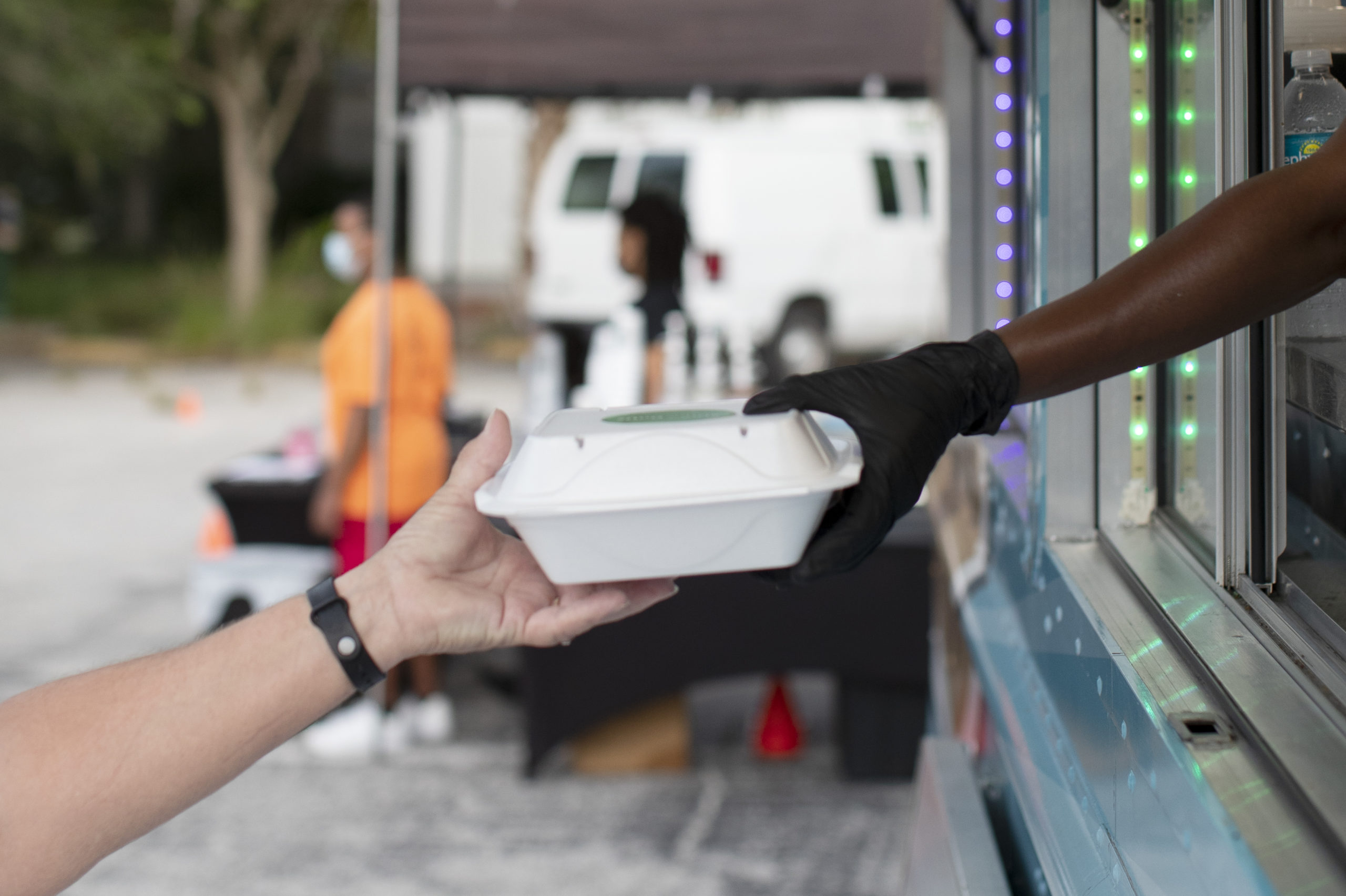 Food service worker wearing a glove hands a food container to a customer during Grow On Us