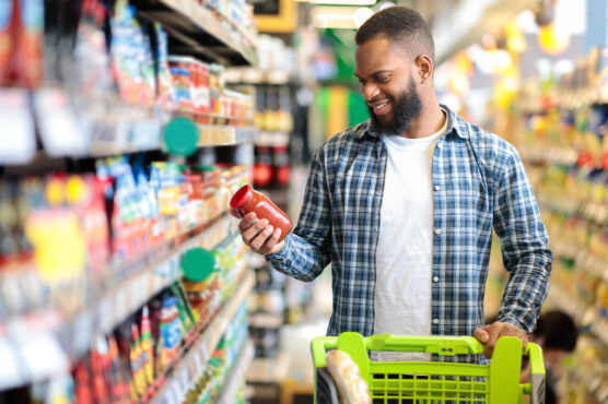 Young man comparing prices and products while grocery shopping with a cart
