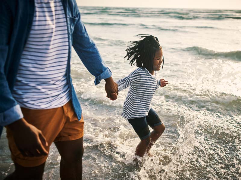 Father and young daughter walking along ocean