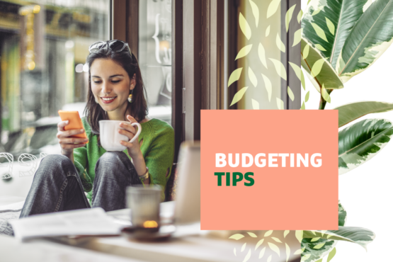 Woman sits at a table smiling while holding a cell phone and a coffee mug with "Budgeting Tips" text overlayed