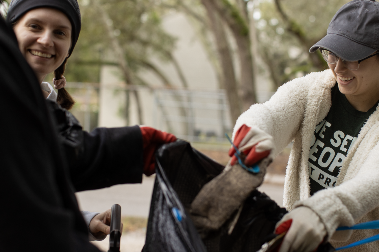 Two smiling women picking up trash in their community.