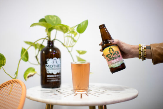 Table with greenery and bottles and glass of kombucha being poured.