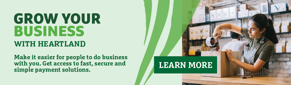 Banner for 'Grow your business' featuring a person taping a box up. Text states, "Grow your business with Heartland. Make it easier for people to do business with you. Get access to fast, secure and simple payment solutions". A 'Log In Now' button is also present.