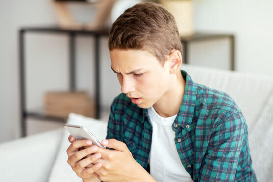 Teenage boy sitting on a sofa and looking intently at his smartphone