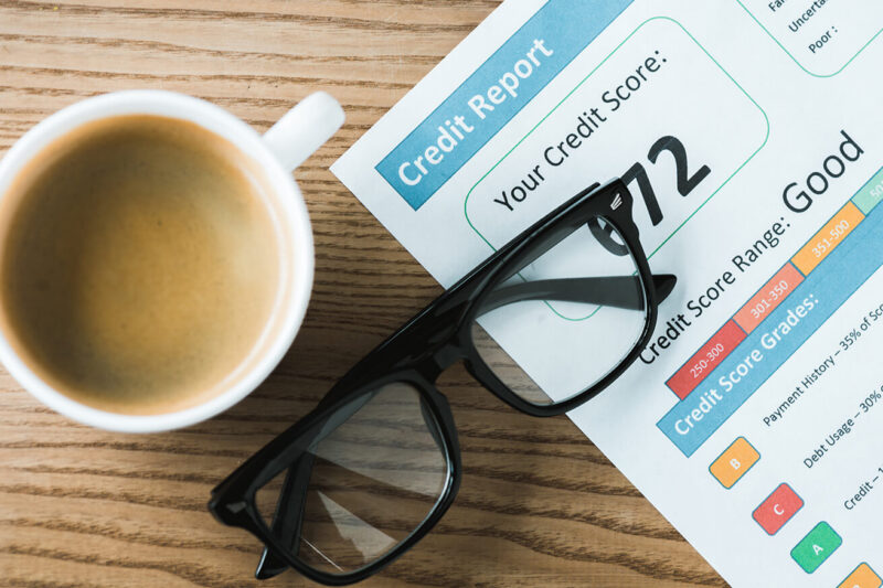A credit score report showing a "Good" rating of 672 next to a cup of coffee and glasses