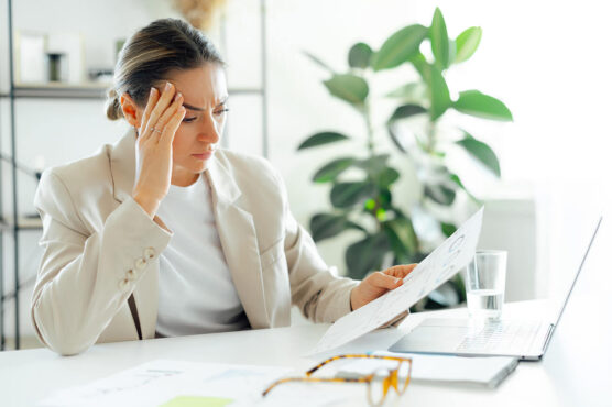 Stressed professional at her desk reviewing financial documents and holding her head in frustration