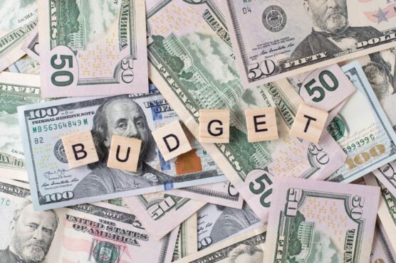 Wooden letter tiles spelling out "BUDGET" scattered over a pile of U.S. dollar bills