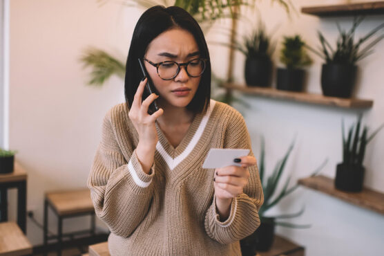 Concerned woman on a phone call holding a credit card in a modern office or cafe