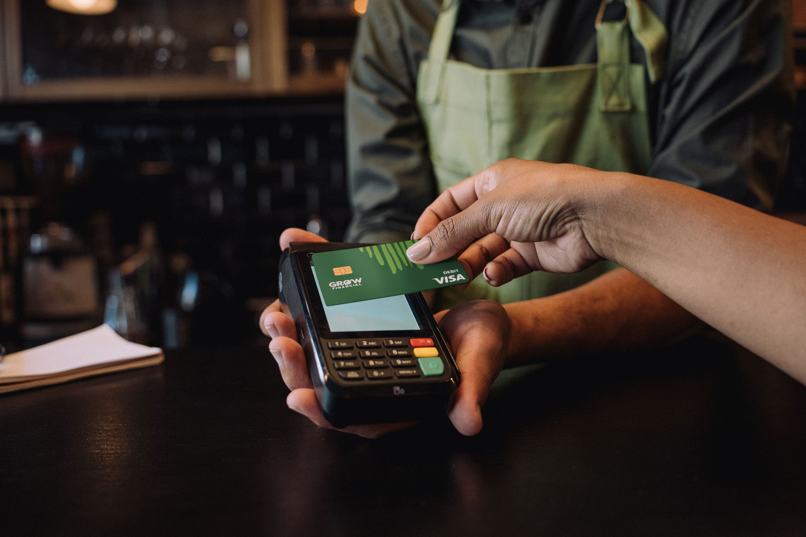 Customer tapping a Grow Visa Debit card on a mobile card reader to pay at a restaurant